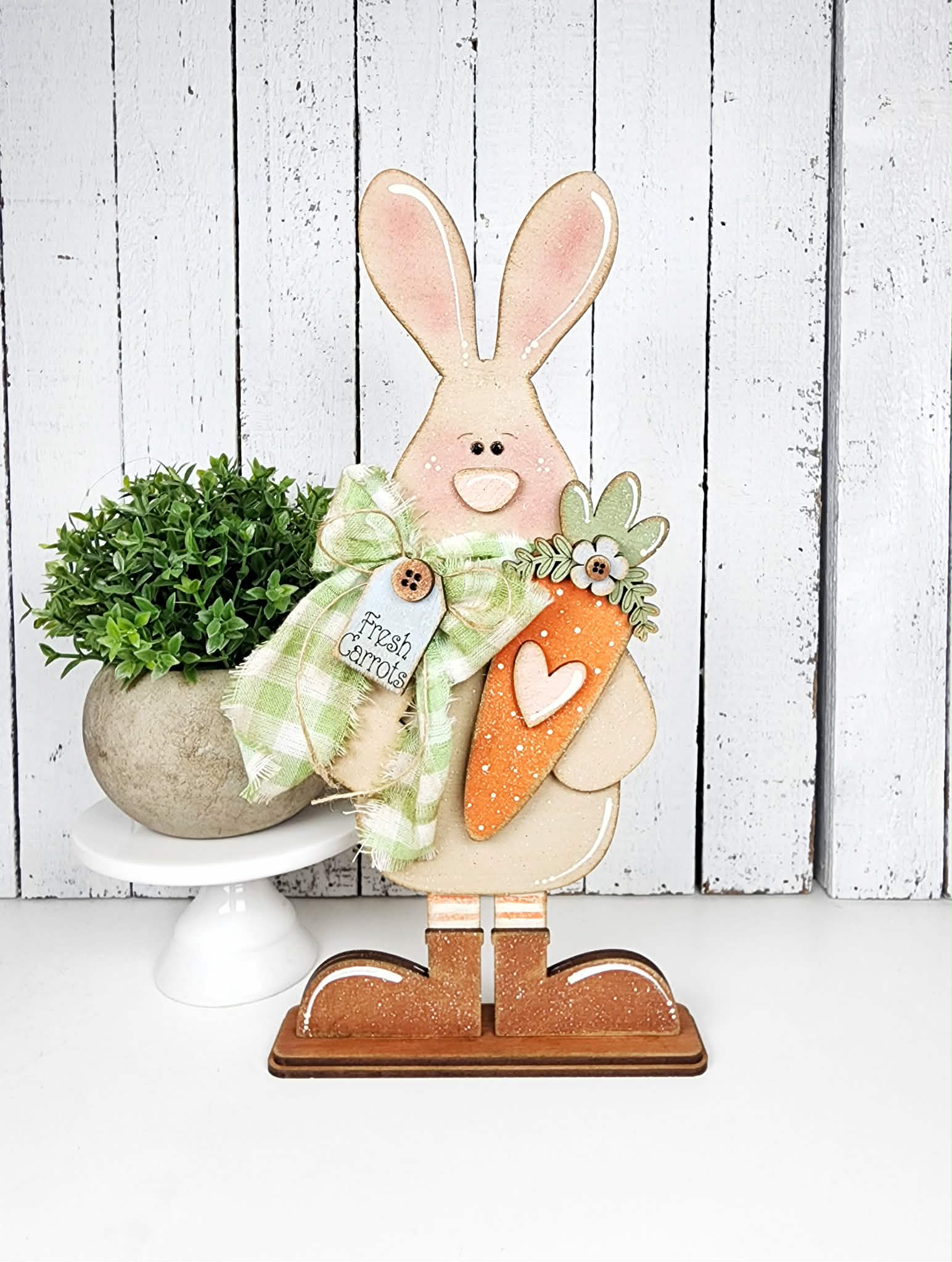 Decorative Easter bunny with a carrot and plant on a white wooden background